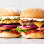 A colorful pair of gourmet burgers showcasing fresh vegetables, sauces, and buns.
