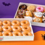 A dozen Original Glazed and an assorted box of decorated doughnuts displayed with ghost and spider Halloween decor
