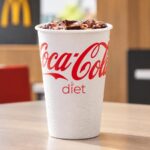 Diet Coca-Cola served with ice in a condensation-covered paper cup inside a McDonald’s restaurant.
