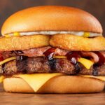 The new Grill Masters Cowboy Angus burger featuring double bacon, cheese, and onion rings on a toasted bun.