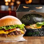 A classic cheeseburger alongside a Halloween burger with a black bun in themed packaging